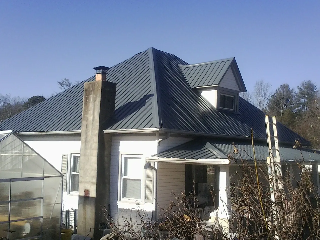Dark blue standing seam metal roof on a white farmhouse with dormer — Slate & Tile Roof Repair by Roofing Brothers in Cheltenham