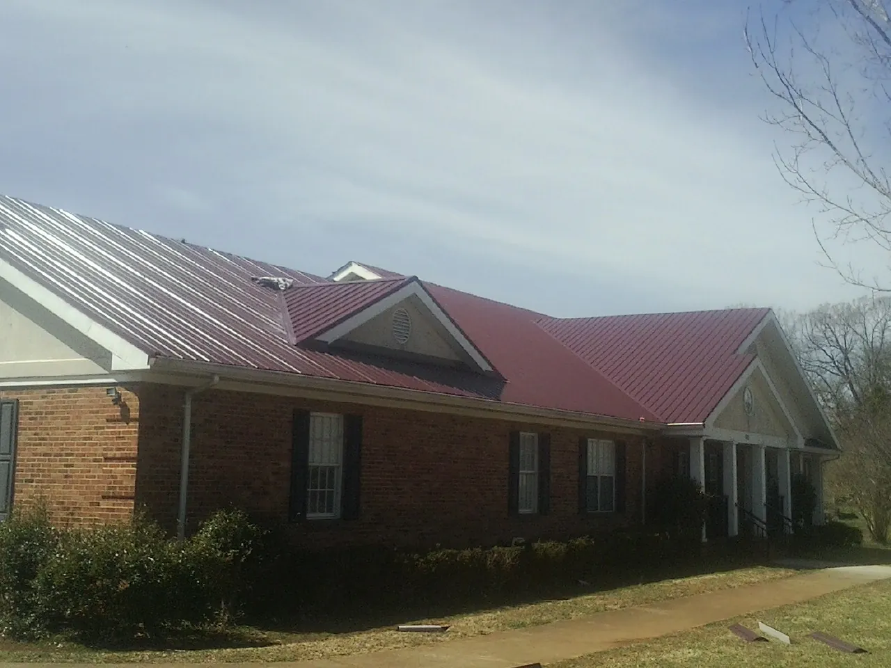 Red metal roof with gabled entries on a long brick building, from a Hail Damage Roof Repair job in Cheltenham