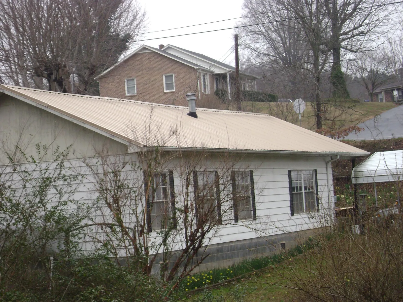 Tan metal roof on a white sided house set into a hillside — Commercial Roofing by Roofing Brothers in Cheltenham